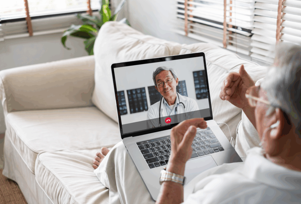Person sitzt auf dem Sofa mit einem Laptop auf dem Schoß und führt ein Videotelefonat mit einem Arzt.
